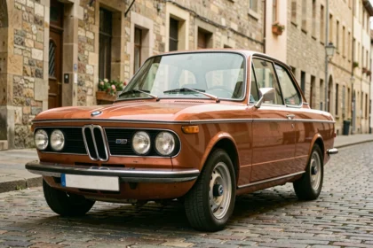 BMW 2002 tii d'occasion en orange Sahara garée sur des pavés européens, vue de face en 3/4, détails authentiques de la carrosserie vintage